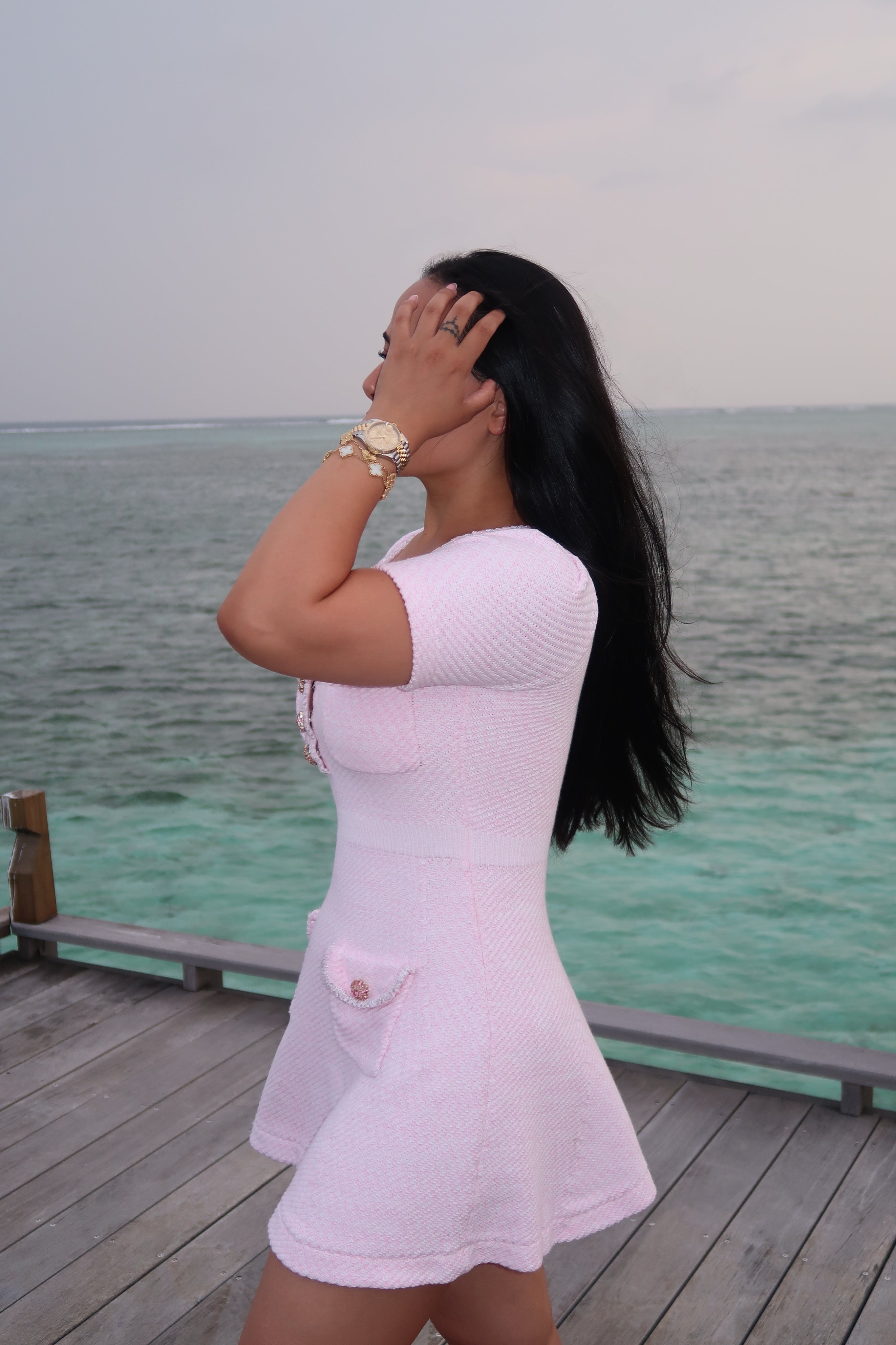 Woman in a pink dress standing on a wooden deck by the ocean.