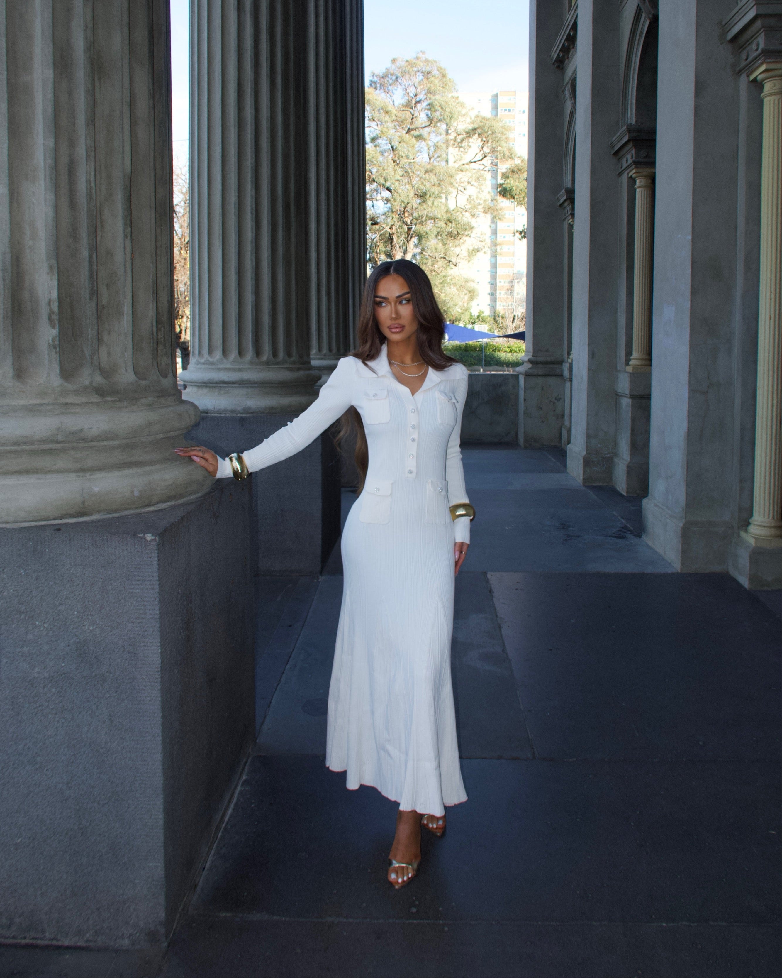 Woman in a white dress standing in an architectural setting with columns.

