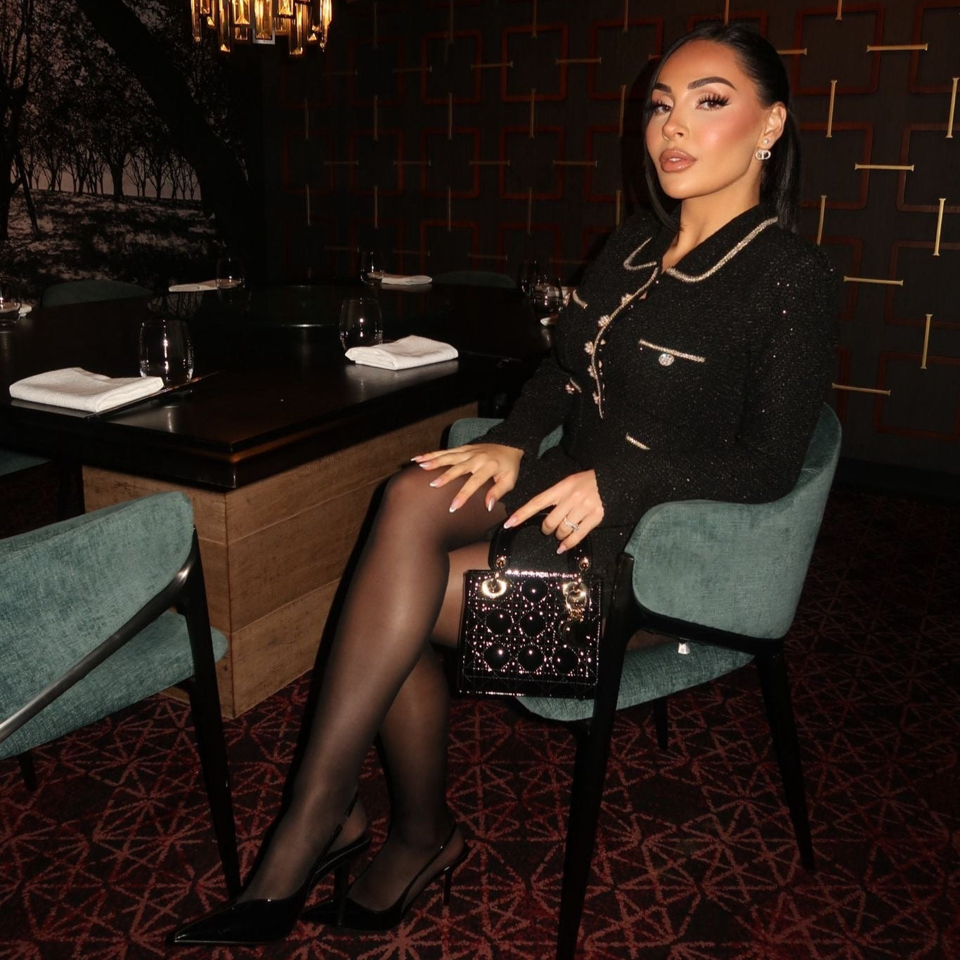 Woman sitting in a stylish chair in a dimly lit room with a chandelier.

